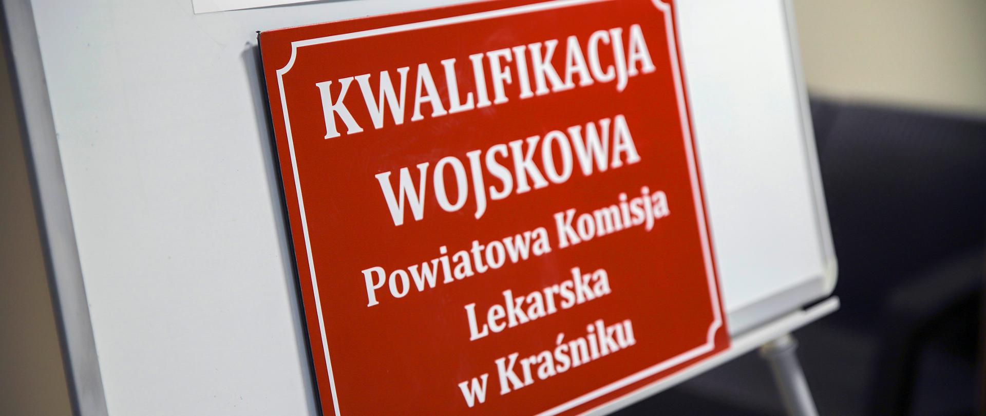 Zdjęcie czerwono-białej tablicy informacyjnej: "Kwalifikacja wojskowa - Powiatowa Komisja Lekarska w Kraśniku".