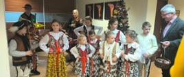Grupa dzieci w strojach góralskich grają i tańczą w sekretariacie urzędu gminy. Obok stoi Zastępca Wójta Gminy Raba Wyżna Mieczysław Kurek