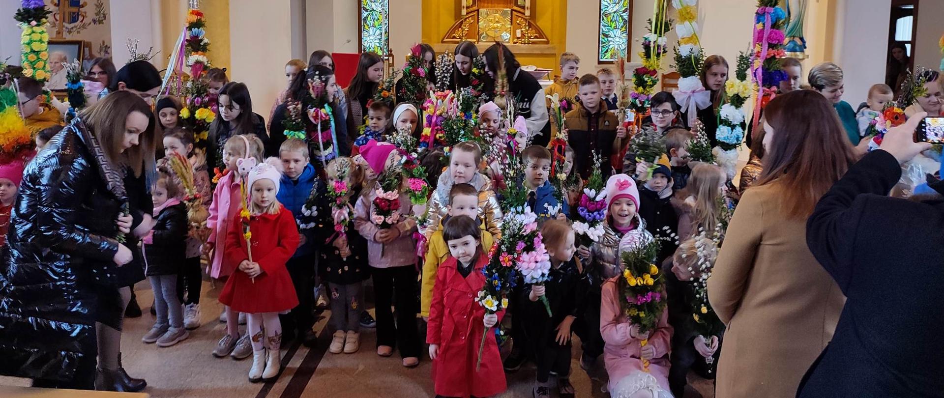 Zdjęcie wykonane w kościele w Podsarniu przedstawia grupę dzieci trzymających palmy wielkanocne