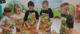 Wspólne pieczenie pierniczków - dzieci siedzą przy stole i wykonują czynności związane z przygotowaniem ciasteczek. Pozują przy tym do zdjęć