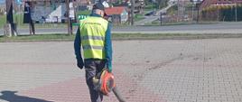 Pan w kamizelce odblaskowej zdmuchuje liście z chodnika dmuchawą do liści