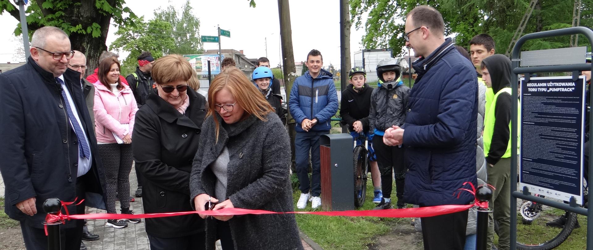 Wspólne przecinanie wstęgi. Przy wstędze stoją 4 osoby. Pozostali uczestnicy stoją z tyłu.