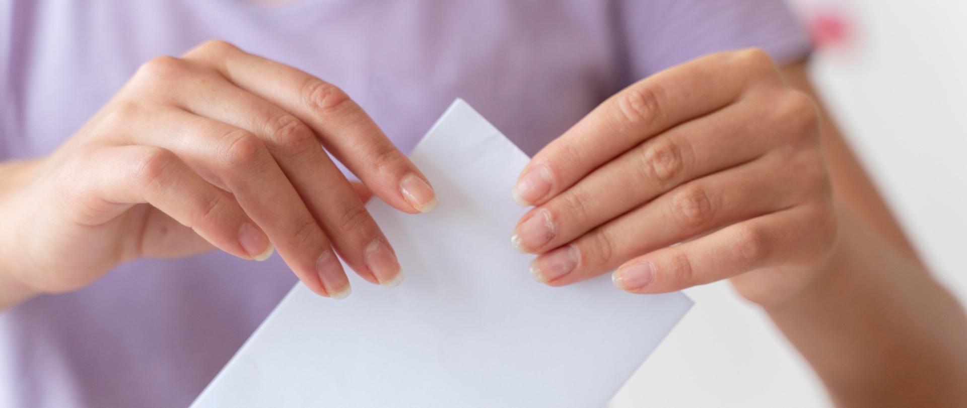 Kobiece dłonie wrzucające kartę do głosowania do urny wyborczej.