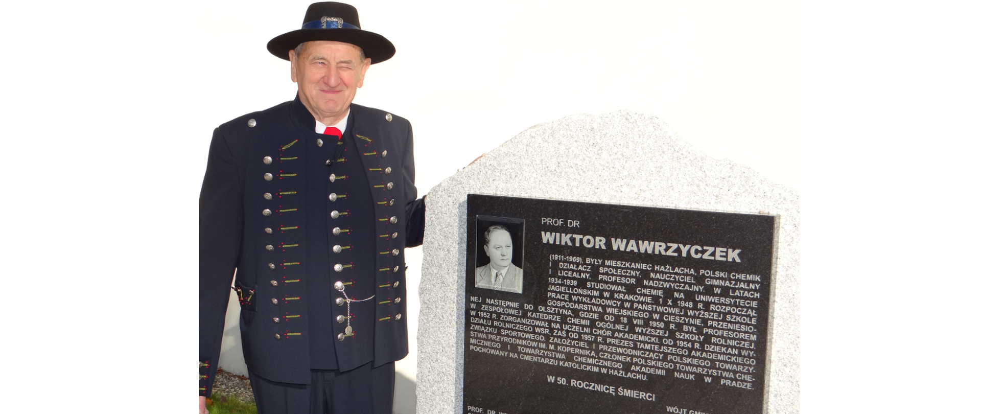 Józef Stoszek przy tablicy upamiętniającej prof. Wiktora Wawrzyczka. Mężczyzna ubrany w cieszyński męski strój ludowy. Na głowie kapelusz. Na tablicy fotografia i biogram W. Wawrzyczka.