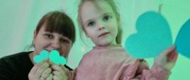 Zajęcia w sali - nauczycielka i dziewczynka pozują do zdjęcia, trzymają papierowe serca