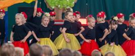 Dzieci w kolorowych strojach tanecznych występują na scenie podczas Festiwalu Kultur. Publiczność ogląda występ z widowni.