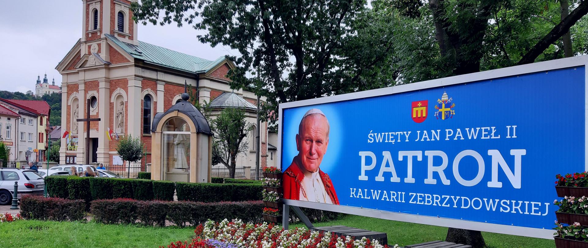 Widok na rynek na pierwszym planie baner - Patron Jan Paweł II, w tle kościół parafialny 