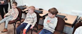 Dzieci siedzą na krzesłach w sali informatycznej