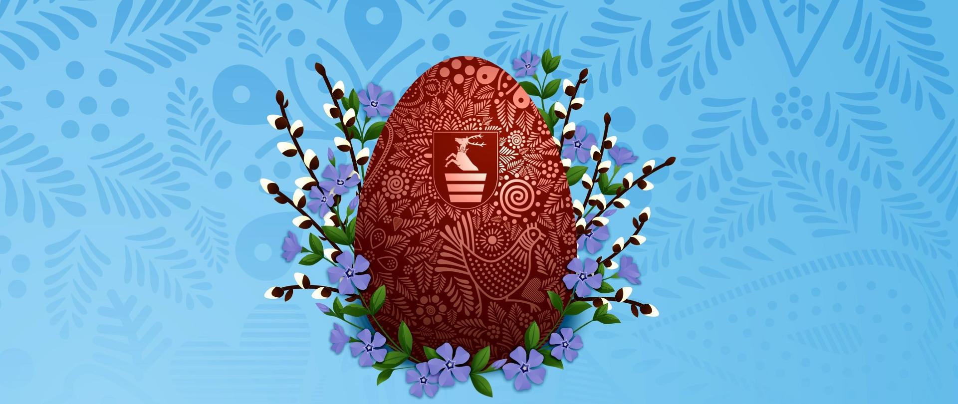 Grafika wielkanocna na jasnoniebieskim tle z delikatnym, roślinnym wzorem ludowym (wycinanką). W centrum znajduje się duże, brązowe jajko wielkanocne (pisanka) bogato zdobione jasnymi, drobnymi ornamentami roślinnymi i wizerunkiem kokoszki. Na środku jajka widnieje herb Powiatu Kraśnickiego. Pisankę otaczają gałązki bazi oraz drobne, fioletowe kwiaty barwnika z zielonymi listkami. Całość ma tradycyjny i elegancki charakter.