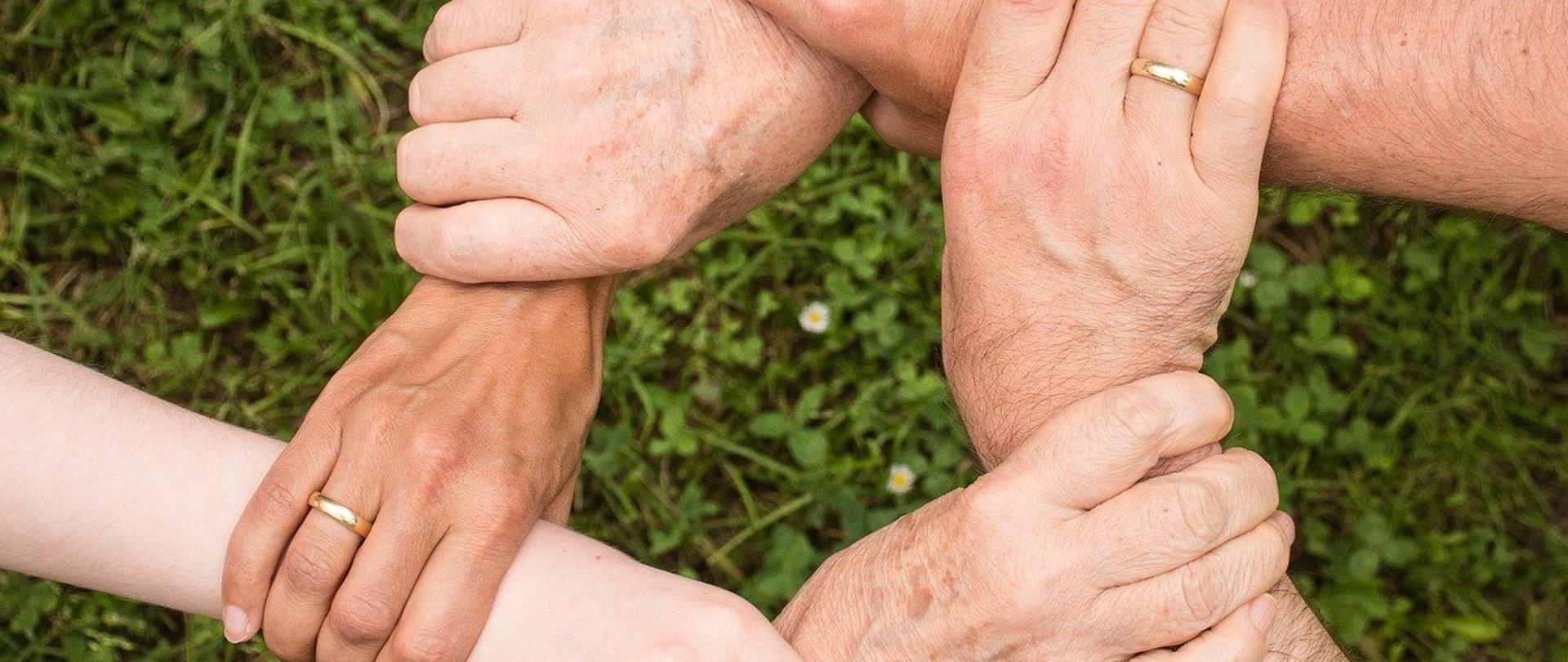 Na zdjęciu splecione mocno i trzymające się razem dłonie sześciu różnych osób