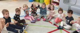 Dzieci siedzą razem w półokręgu, trzymają się za ręce