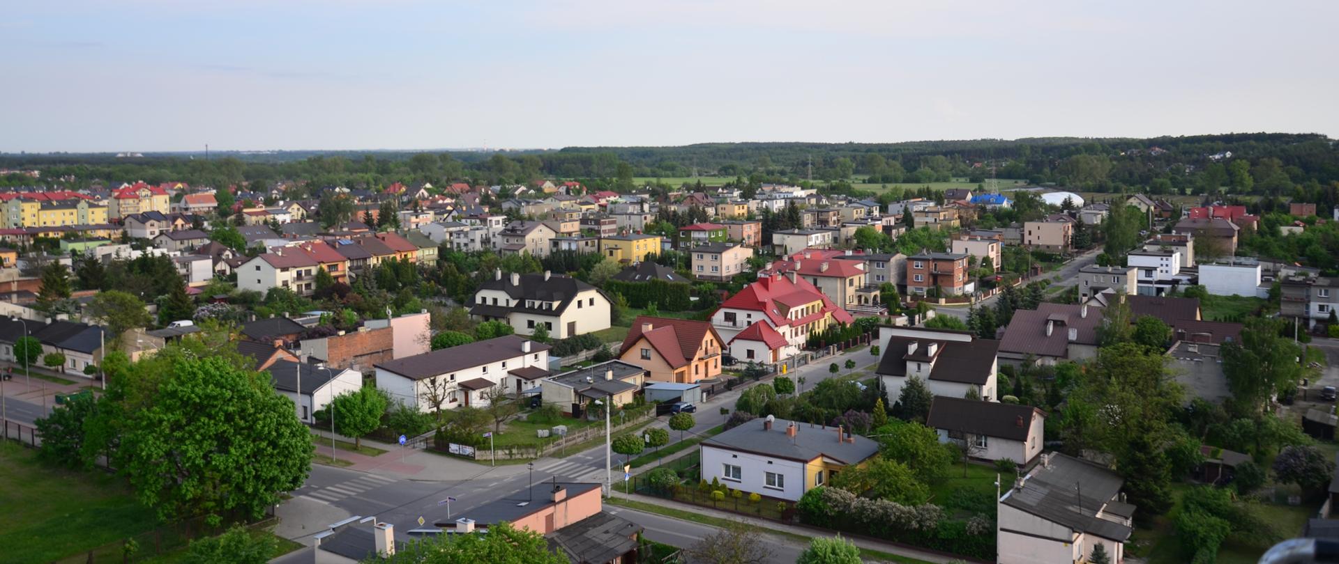 Widok z góry na osiedle domków jednorodzinnych, na dole widoczne skrzyżowanie dwóch ulic, u góry błękitne niebo.