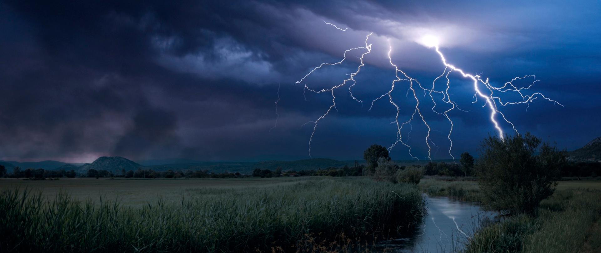 Burza nad rzeką, ciemne chmury, piorun uderza w ziemię