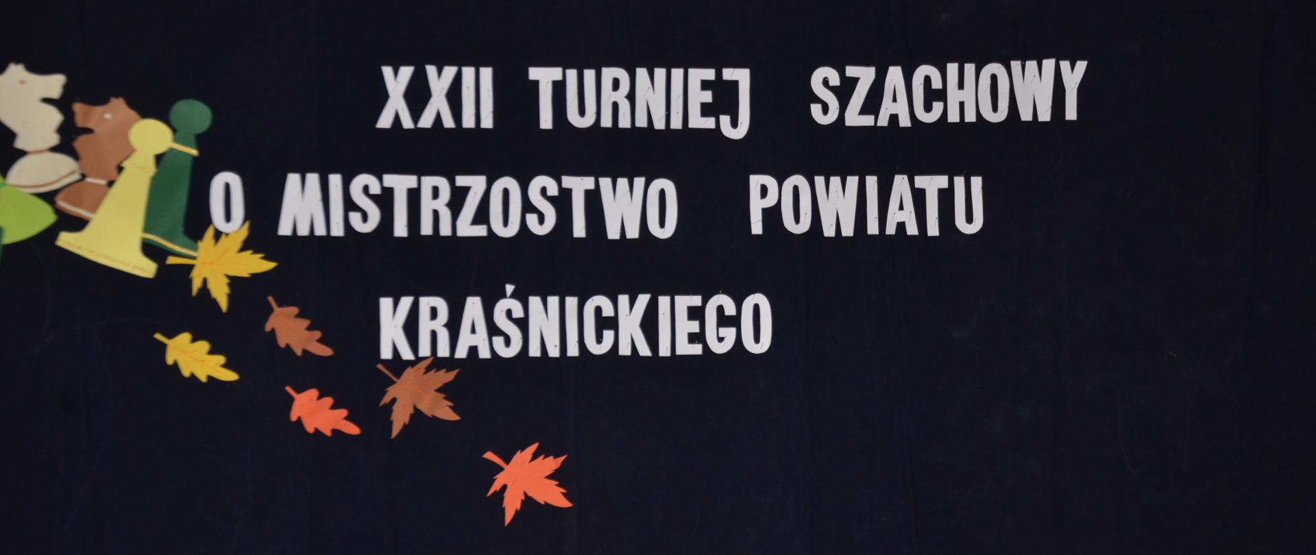 Biały napis na czarnej tablicy: XXII Turniej Szachowy o Mistrzostwo Powiatu Kraśnickiego