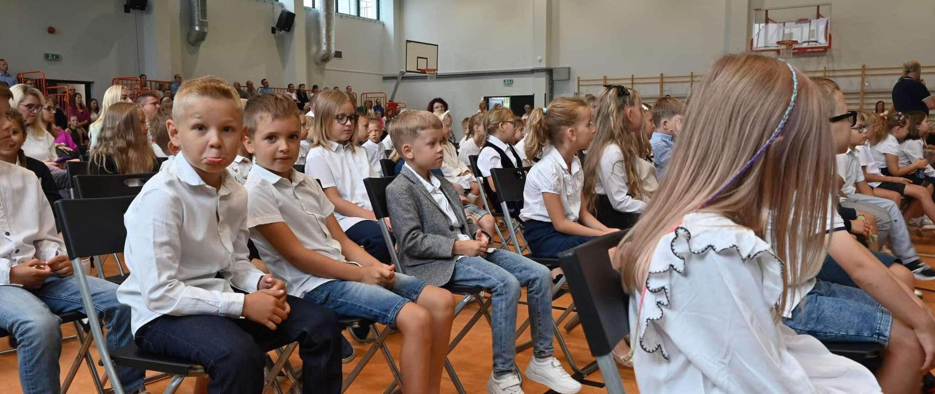 dzieci siedzące podczas rozpoczęcia roku szkolnego na hali