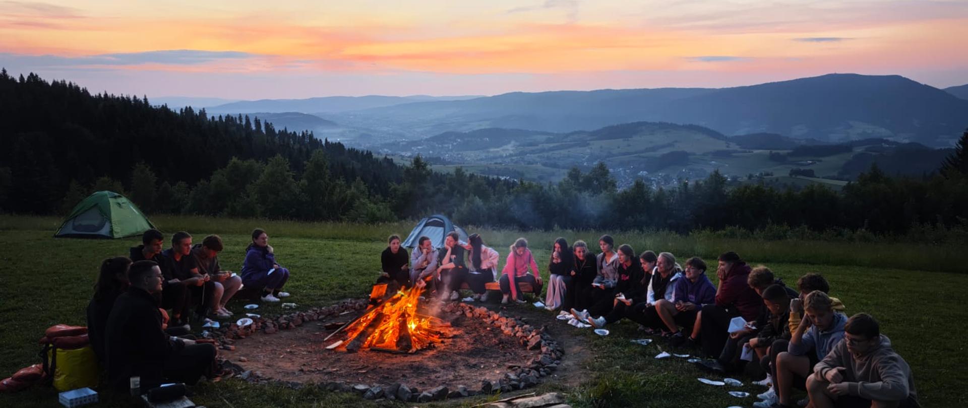 Wszyscy uczestnicy zielonej szkoły wspólnie przy ognisku podczas zachodu słońca. 