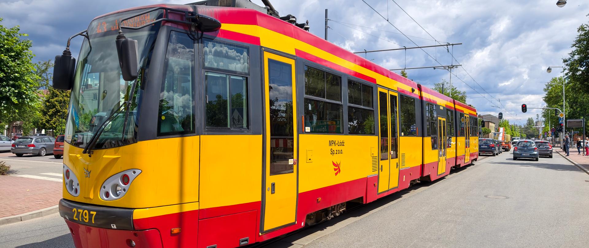 Żółto-czerwony tramwaj linii 43 jadący w kierunku Konstantynowa Łódzkiego. Na elektronicznym wyświetlaczu widoczny jest kierunek „KONSTANTYNÓW ŁÓDZKI – Plac Wolności”. Tramwaj porusza się ulicą wśród zabudowy miejskiej.