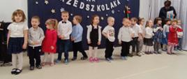 Przedszkolaki stoją w sali na tle ścianki "Pasowanie na przedszkolaka"