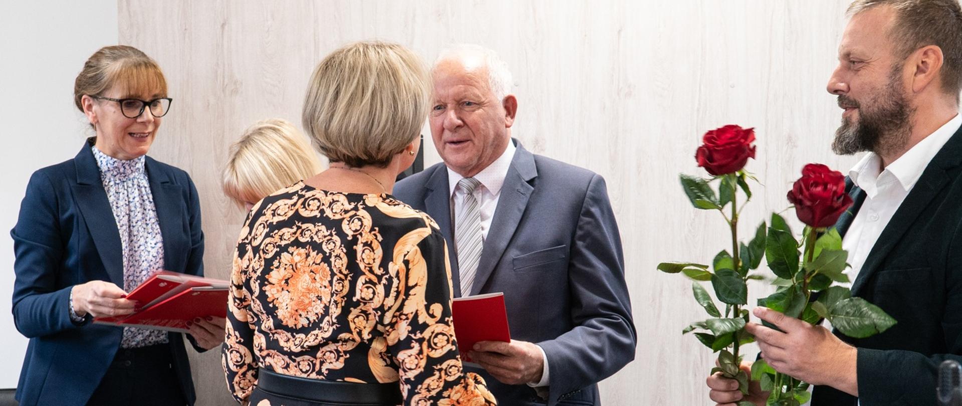 Burmistrz wręcza nagrodę dyrektorce szkoły, obok niego radny trzyma dwie róże.