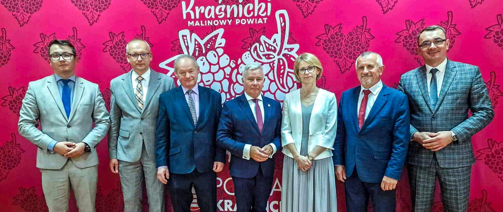 Zdjęcie przedstawia stojących w rzędzie członków Zarządu Powiatu, pozujących do zdjęcia na tle ścianki.