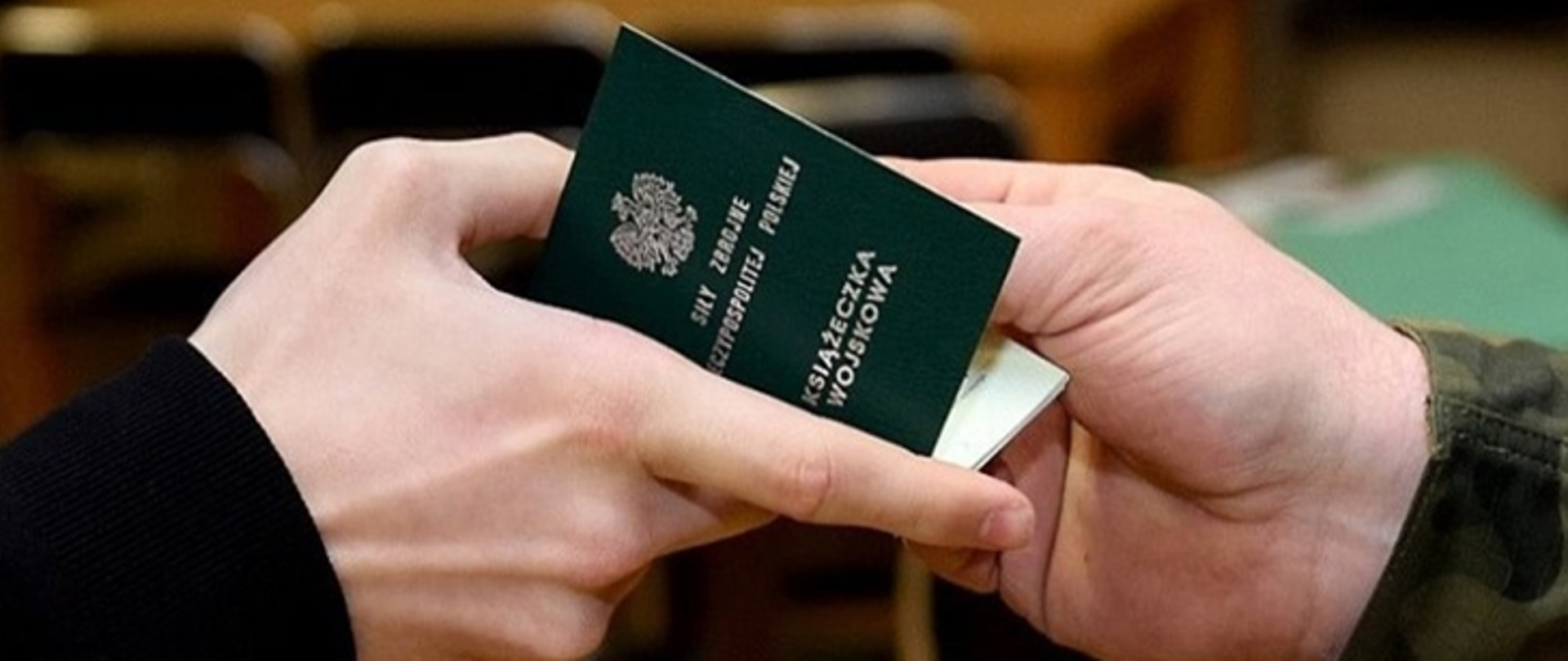 Ręce przekazujące sobie zieloną książeczkę z orłem i napisem Książeczka wojskowa