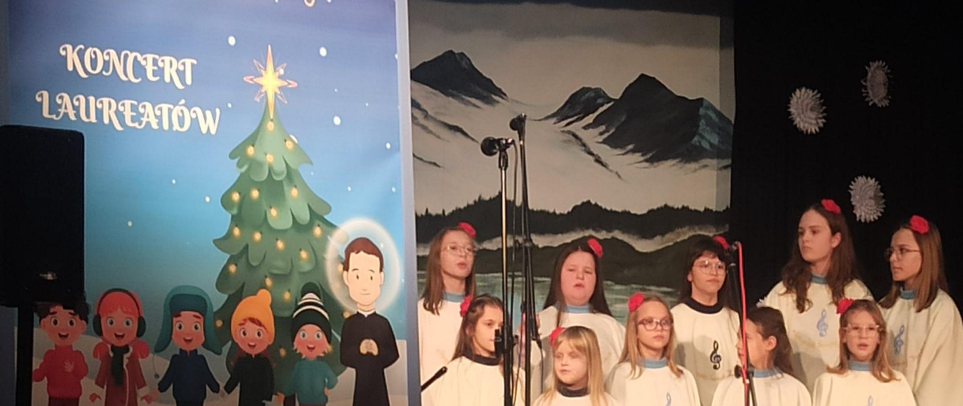 Koncert finałowy laureatów konkursu kolęd w Skawie.Po lewej stronie zdjęcia widać plakat Konkurs Laureatów, na środku występujących uczestników.