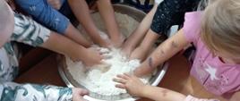 Warsztaty kulinarne - dzieci stoją przy stole ze składnikami, mieszają ciasto