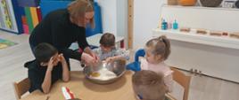 Wspólne pieczenie pierniczków - dzieci siedzą przy stole i wykonują czynności związane z przygotowaniem ciasteczek. Pozują przy tym do zdjęć