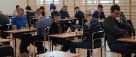Zawodnicy siedzący na krzesłach podczas pojedynków szachowych przy ustawionych w rzędach stołach na hali sportowej podczas XXIII Otwartego Turnieju Szachowego o Mistrzostwo Powiatu Kraśnickiego w 2023 roku.