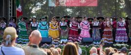 Zespół folklorystyczny z Meksyku w kolorowych tradycyjnych strojach i sombrero przed publicznością, na scenie plenerowej podczas Międzynarodowego Festiwalu Folklorystycznego Polka w Konstantynowie Łódzkim. Za nimi na dużym banerze widnieje informacja o festiwalu. 