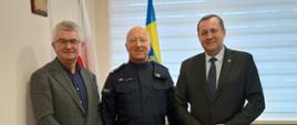 Trzech mężczyzn w pozycji stojącej, od lewej zastępca wójta Mieczysław Kurek w środku Nowy Komendant w mundurze policyjnym a od prawej Wójt Gminy Raba Wyżna w tle flaga polski oraz flaga z herbem urzędu gminy 