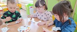 Kreatywne zajęcia artystyczne - dzieci siedzą przy stole, malują wycinanki w kształcie kotów
