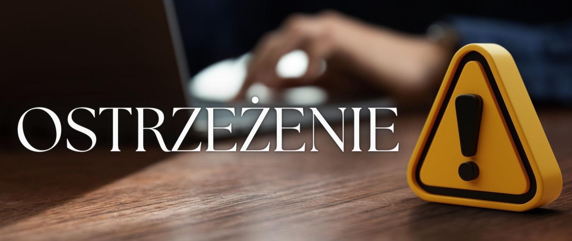 Na pierwszym planie biały napis ostrzeżenie, z prawej strony w żółtym trójkącie czarnym wykrzyknik. Na drugim planie rozmazana postać z laptopem. Napis i wykrzyknik umieszczone są na ciemnobrązowym biurku. 