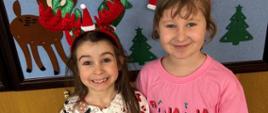Dwie dziewczynki pozują do zdjęcia, mają na głowie świąteczne czapki
