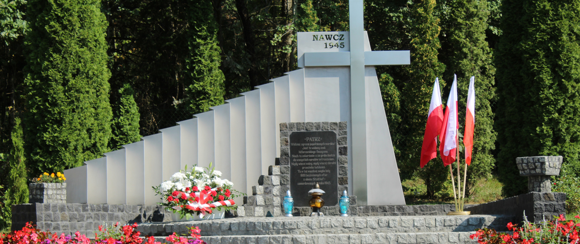 Zdjęcie pomnika ofiar Marszu Śmierci KL Stutthof ze złożonymi kwiatami na tle lasu