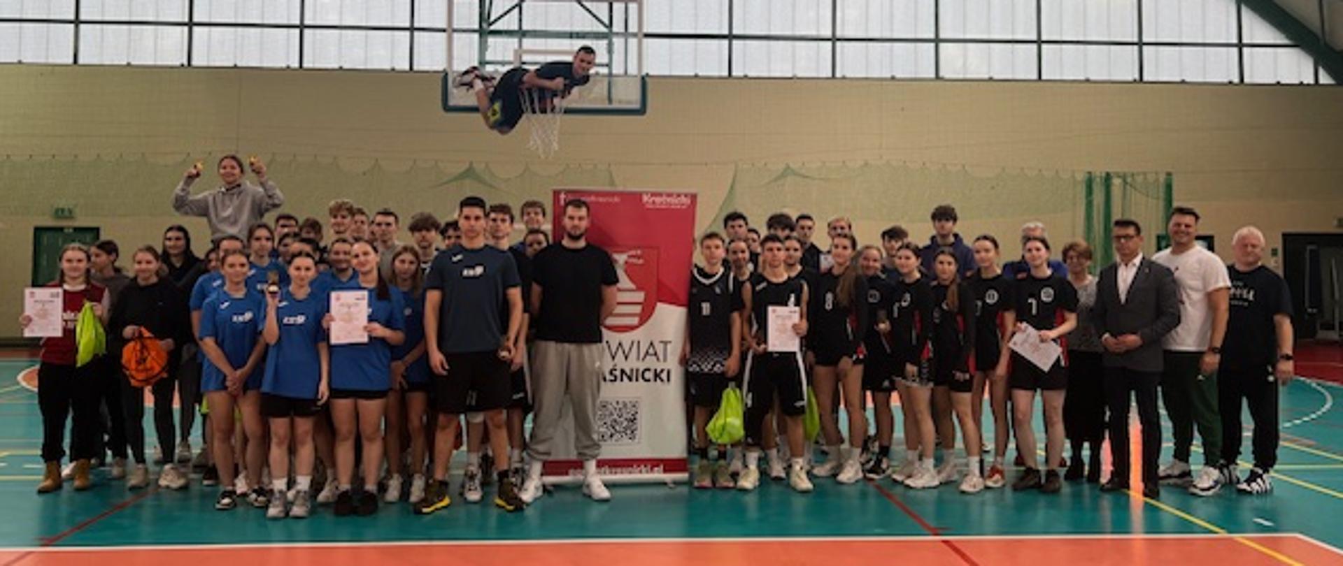 Uczestnicy turnieju wraz z nagrodami i dyplomami, opiekunami i organizatorami. Pośrodku zawodników stoi biało-czerwony rollup Starostwa Powiatowego w Kraśniku.