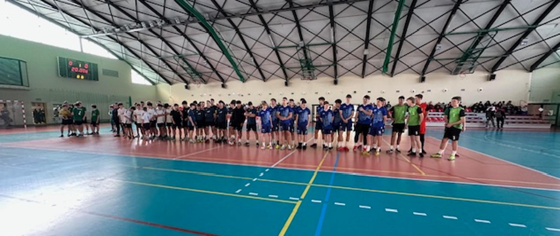 Uczestnicy turnieju stoją w szeregu na środku hali sportowej