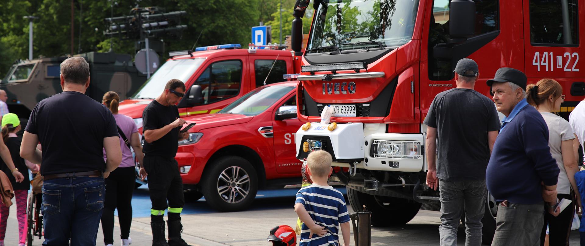 Zdjęcie przedstawia ludzi oglądających wystawę samochodów strażackich.