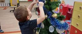 Chłopczyk stoi przy choince, dekoruje ją