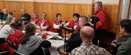 Koło Gospodyń Wiejskich w tradycyjnych chustach góralskich na barkach. Grają na gitarach i śpiewają kolędy. 