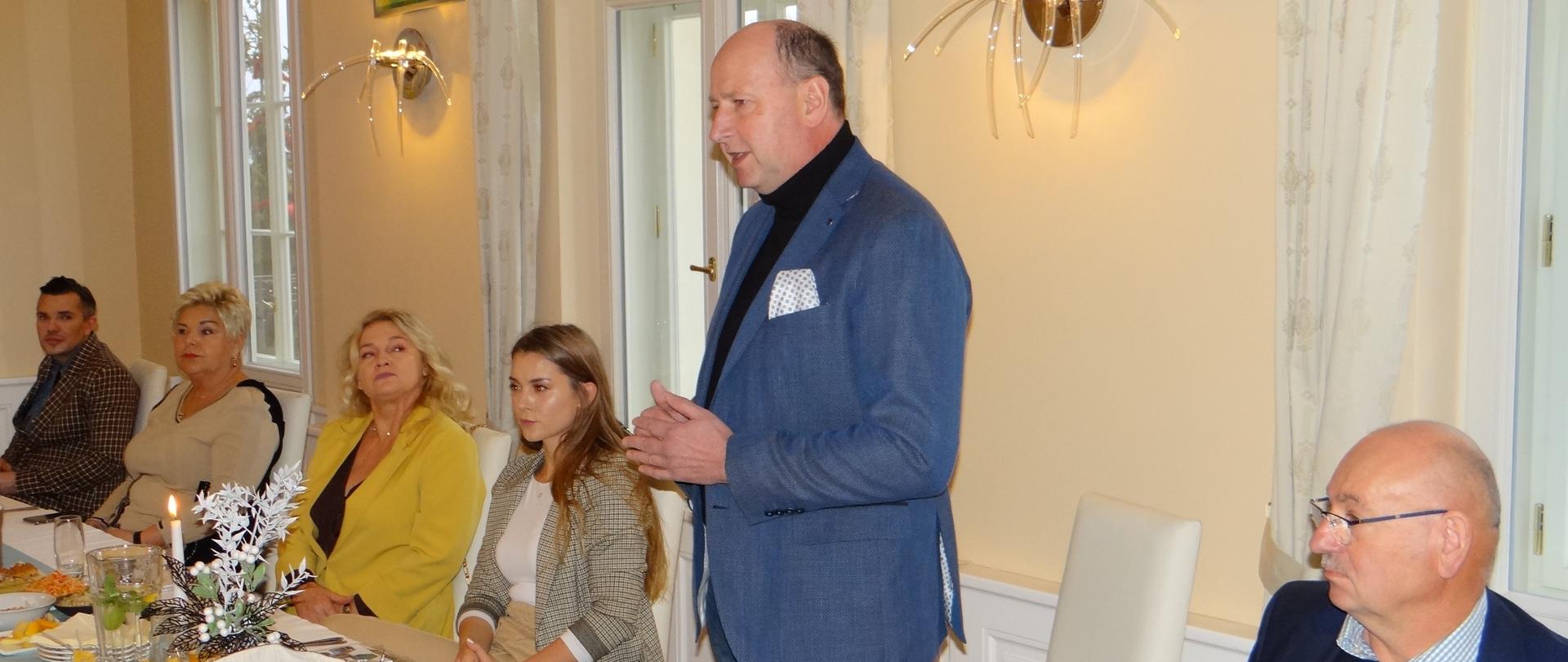 Głos podczas spotkania zabiera Marcin Lipski, prezes Stowarzyszenia „Cieszyński Szlak Wina”. Pięć osób siedzi za stołem, szósta (mężczyzna) stoi i przemawia.