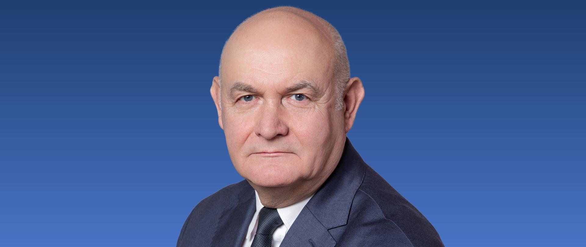 Zdjęcie przedstawia mężczyznę w krawacie na niebieskim tle.