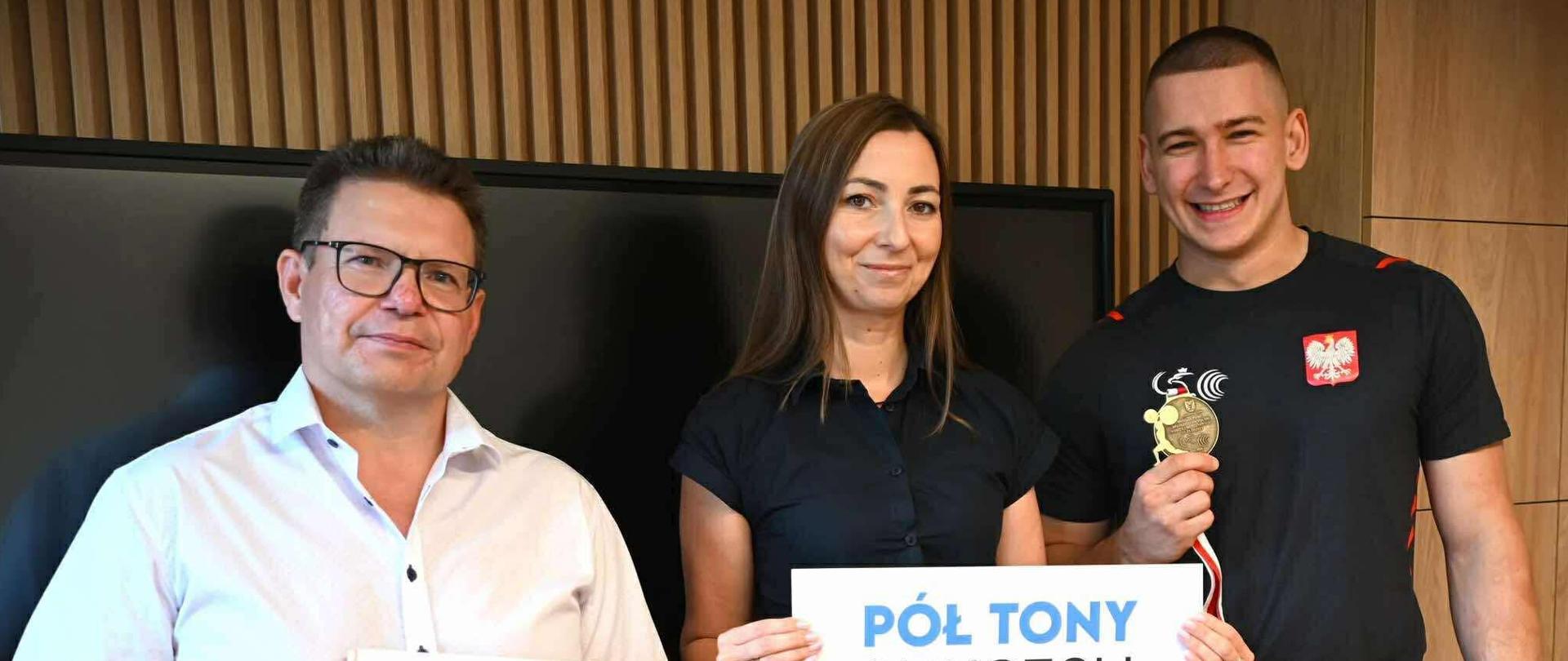 Widok na dwóch zawodników odbierających nagrodę oraz osobę wręczającą. 