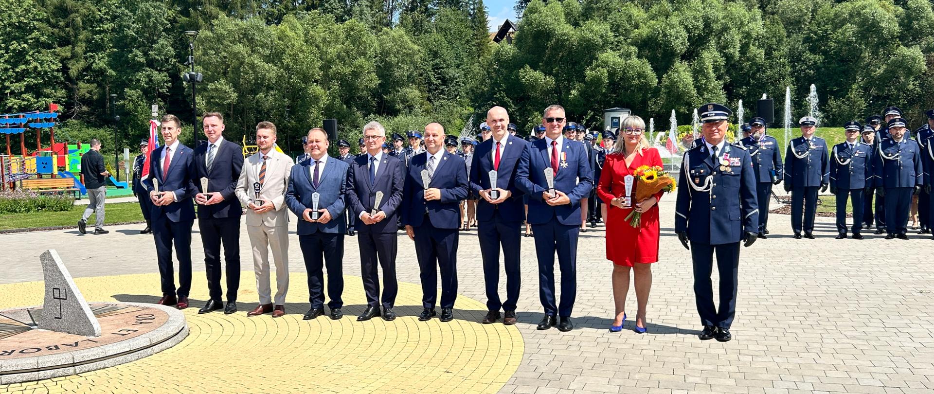 Grupa osób stojących na placu podczas oficjalnej części wydarzenia.