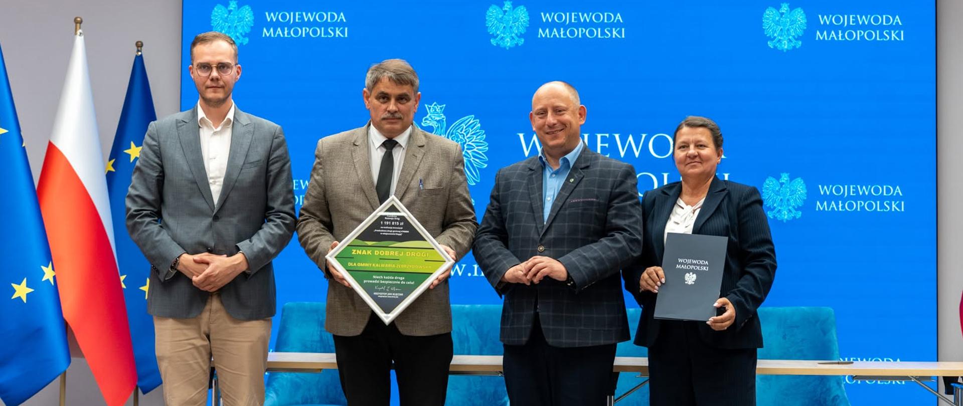 Przedstawiciele województwa i gminy pozują do zdjęcia, za nimi flagi Polski i Unii Europejskiej i stół, przy którym podpisano umowę