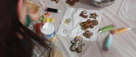 Uczestnicy warsztatów siedzą przy stole, dekorują pierniczki