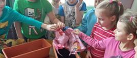 Dzieci przygotowują ogródek - stoją przy stole, na którym stoją donice i nasiona. Trwa akcja sadzenie