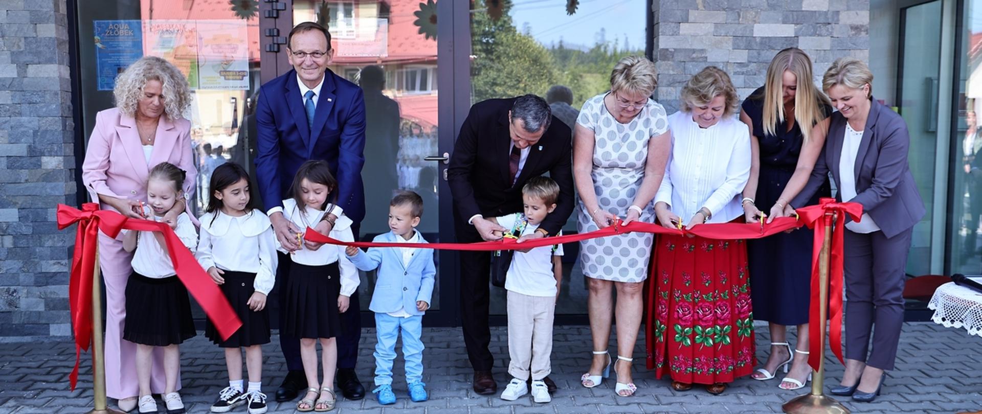Przecięcie wstęgi na otwarcie nowego budynku przez zaproszonych gości oraz przedszkolaków.