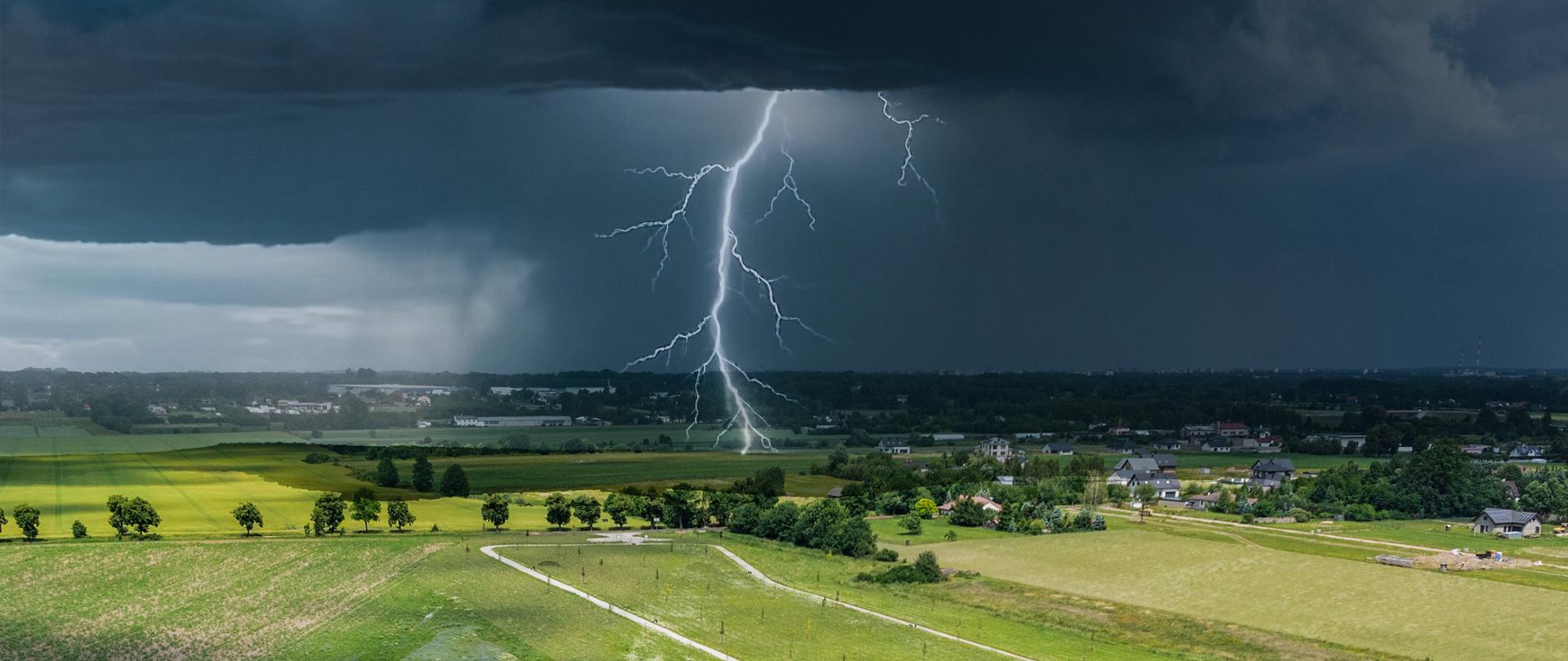 Burza nad polami. Ciemne chmury, w centralnej części błyskawica sięgająca ziemi.