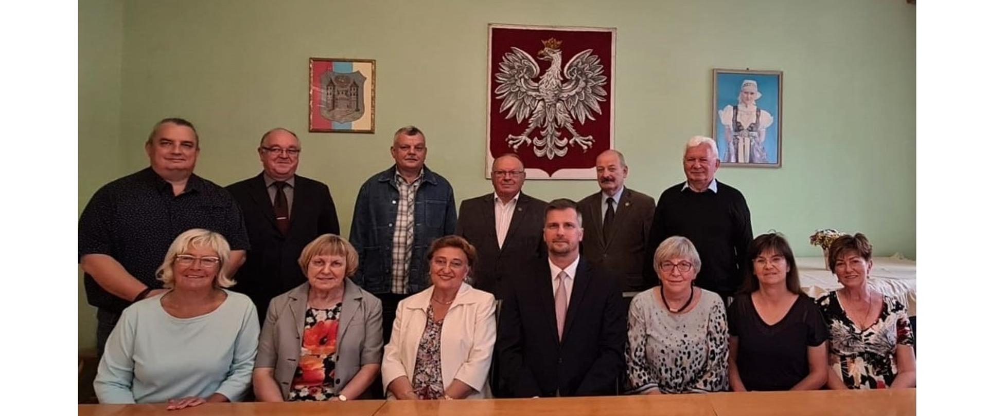 Nowy Zarząd Główny Macierzy Ziemi Cieszyńskiej. Pierwszy szereg siedzi, drugi stoi. Z tyłu na ścianie herb Cieszyna, godło państwowe i fotografia kobiety w stroju cieszyńskim